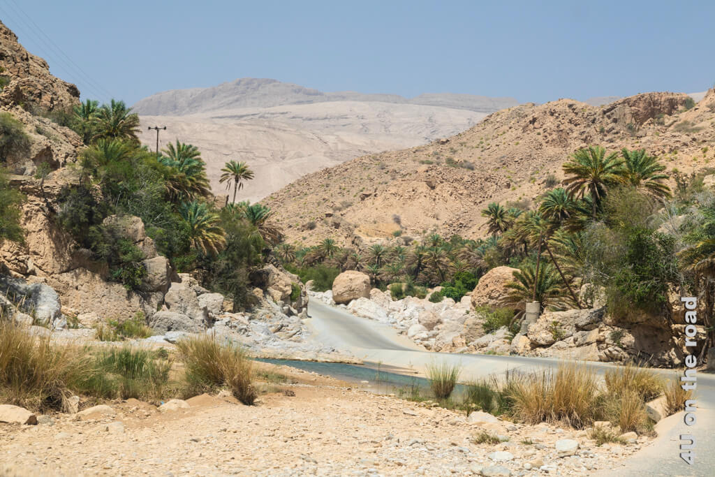 Die Anfahrt zu den Pools des Wadi Bani Khalid führt durch ein Tal in den Bergen mit runden Felskugeln und grünen Palmen.