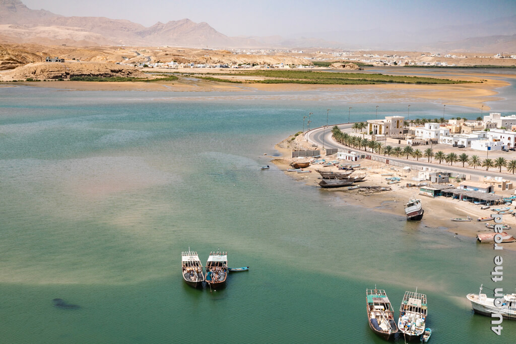 Der Fjord, an dem die Stadt Sur im Oman liegt, zieht sich weit ins Hinterland. Dhaus liegen paarweise im Wasser und warten auf die Flut. Im Hintergrund erheben sich hohe Berge.