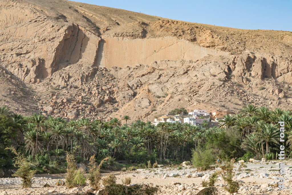 Unterhalb von steilen Felsen steht ein Dorf auf einer Art Schüttkegel im Canyon des Wadi Bani Khalid. Zu Füssen des Dorfes wächst ein Palmenhain.